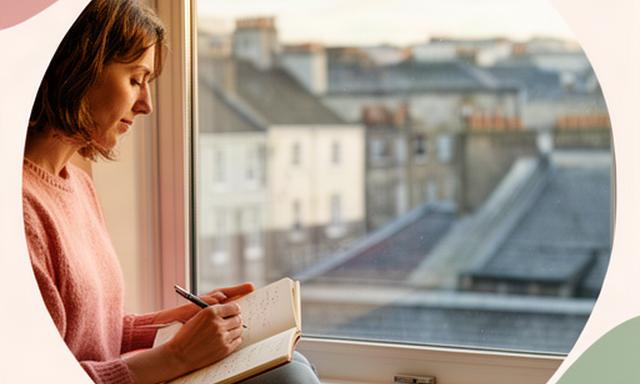 Person writing in a notebook beside a window overlooking Dublin rooftops while settling into a new home